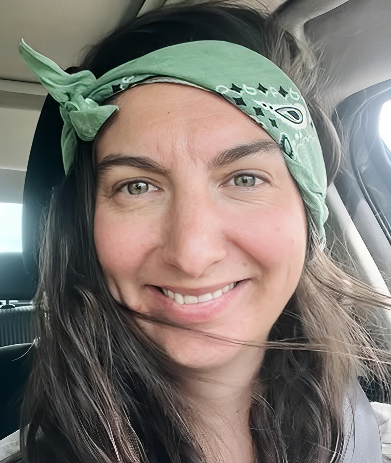 Woman with a green bandana smiling inside a car.